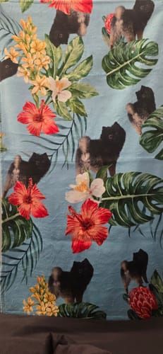Ein Kunde zeigt sein personalisiertes Strandtuch mit einem Muster aus Hundefotos und tropischen Blumen.