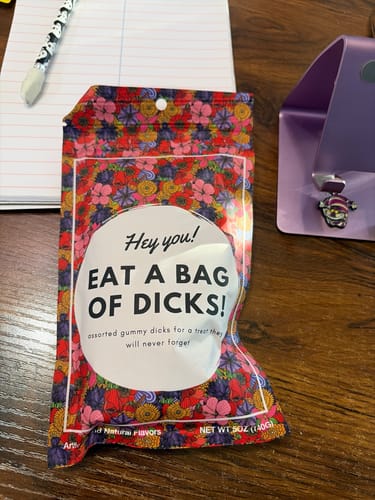 Reviewer's 'Bag of Dicks' candy in its colorful floral pouch, sitting on a desk next to a notebook.
