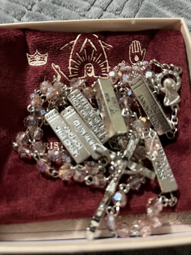 Customer's Mysteries Rosary with pink beads and engraved bars resting on a red pouch in its box.