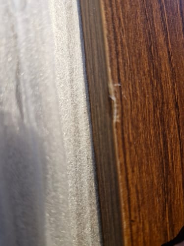 Close-up door een klant van een gerafelde, beschadigde rand van het walnootkleurige dressoir.