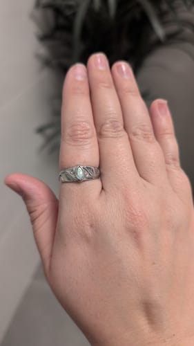Close-up of a customer's hand wearing the silver October Birthstone Ring with its detailed leaf-design band and opal.