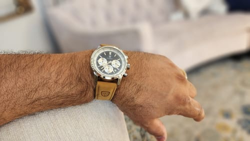 Customer's wrist showing the Lucky Fours® Meridian watch with a black chronograph face and a tan leather strap.