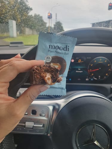Customer holding a half-eaten Choc Caramel Plant Protein Ball, showing its caramel center, with packaging visible in a car.