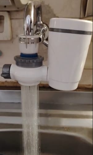Cliente muestra su Power Filtro instalado en un grifo, con agua fluyendo directamente al fregadero.