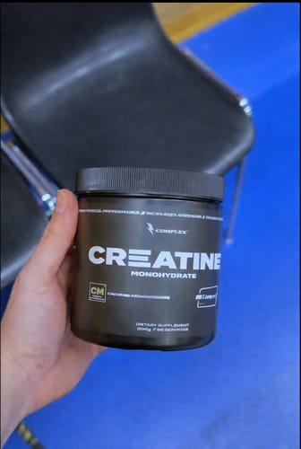 Reviewer holding a black tub of Creapure Creatine supplement against a blue and black background.