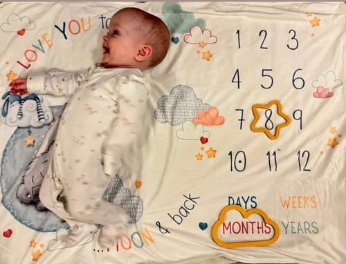 Reviewer's photo of a baby on a milestone blanket, who will wear an item from the knitting kit.