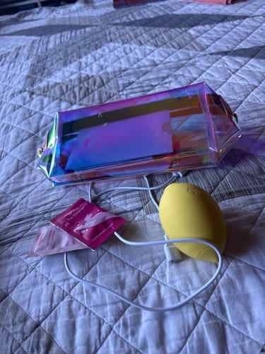 Customer's holographic Pleasure Pouch on a bed next to a yellow toy and charging cable.