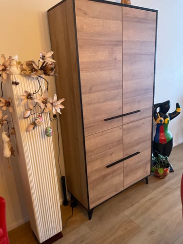 Klant toont de licht eiken Opbergkast Frey met 4 deuren en zwarte handgrepen in een kamer.