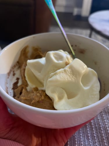 Reviewer's bowl of protein mug cake with a dollop of Birthday Cake Peanut Butter Spread and cream on top.
