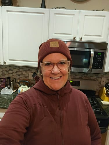 Reviewer in a kitchen wearing the Zoey Zip Up Hoodie in Toasted Garnet, zipped high to the chin for warmth.