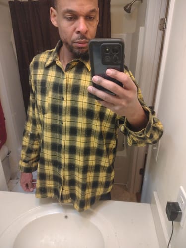 Customer in a mirror selfie wearing the black and yellow flannel long sleeve shirt.