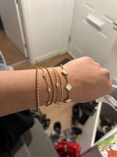 Customer's wrist with a stack of several gold-colored bracelets indoors.