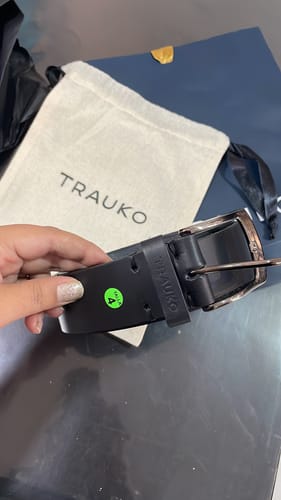 Primer plano de la mano de un cliente sosteniendo el Cinturón Casual Negro por la hebilla.