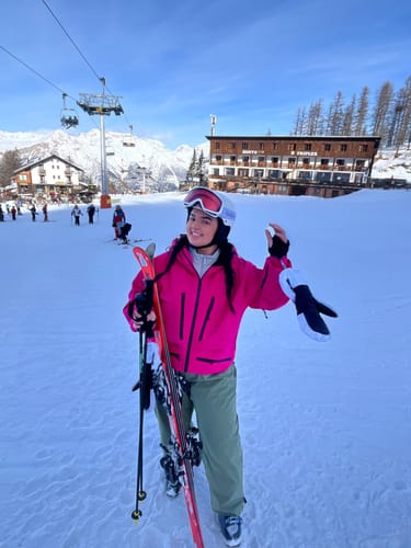 Reviewer smiling on a snowy mountain slope wearing the baggy drawstring snow pants with a pink jacket.