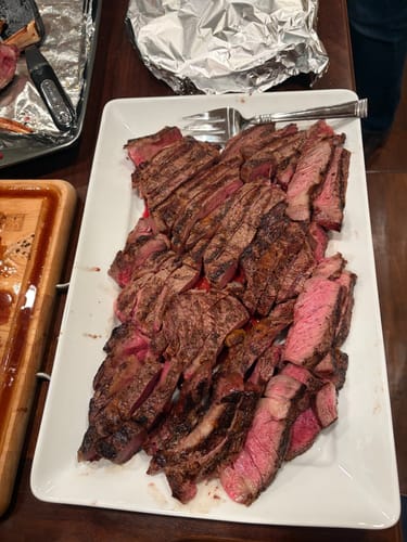 Customer's cooked Choice Bone-In Ribeye, sliced on a white platter showing a juicy, medium-rare center.
