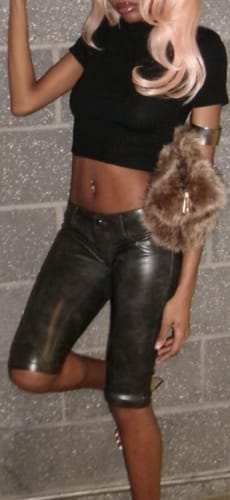 Reviewer posing in the low-rise black Leather Capris against a grey brick wall.