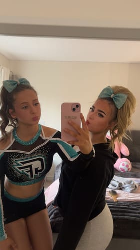 Reviewer on the right wearing the Stranded Clip-in Ponytail styled high with a large sparkly cheer bow.