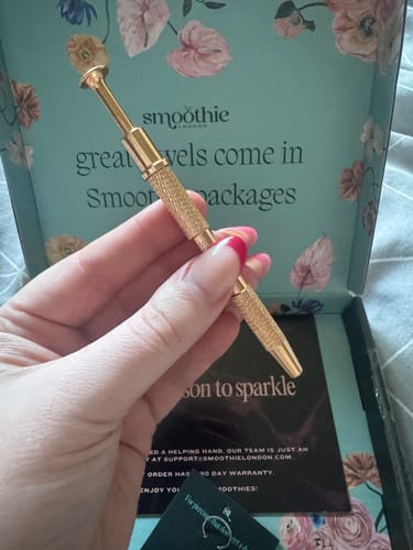 Reviewer's hand holding the gold-toned Flatback Grabber tool as it grips a small flower-shaped earring.