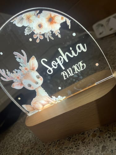 Kundenfoto des leuchtenden, personalisierten Nachtlichts mit Reh-Motiv, das mit dem Namen 'Sophia' und einem Datum graviert ist.