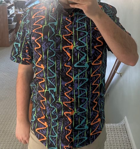 Reviewer taking a mirror photo wearing the 'Retro Squigglies' short sleeve shirt, showing its colorful pattern and fit.