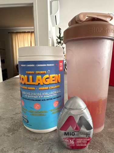 Pot de Collagène marin de Yummy Sports d'un client à côté d'un shaker et d'un rehausseur d'eau Mio sur un comptoir.