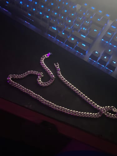 Un cliente muestra su brillante Cadena Cuban Link sobre un escritorio oscuro junto a un teclado.