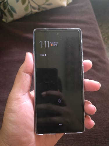 Reviewer holding a smartphone with the UltraShield Tempered Glass installed, showing a clean, bubble-free application.