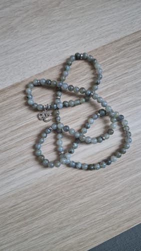 Le bracelet mala en labradorite d'un client, enroulé sur une surface en bois.