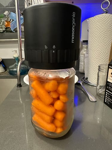 Customer using the black Mason Genie Vacuum Sealer on a glass jar full of carrots on a kitchen counter.