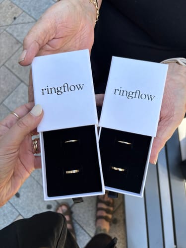 Customers holding two open ring boxes, each displaying two gold rings made during their Sparked experience.