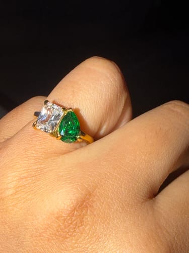 Close-up of a reviewer wearing the Toi Et Moi Birthstone Ring, showing the green pear-cut and clear emerald-cut stones.
