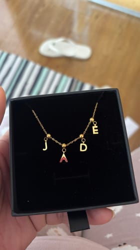 Customer holding a black box showing a gold Name Letters necklace spelling 'JADE'.