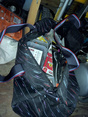 Customer's CASH DUFFLE BAG open and filled with various work tools and supplies in a garage.