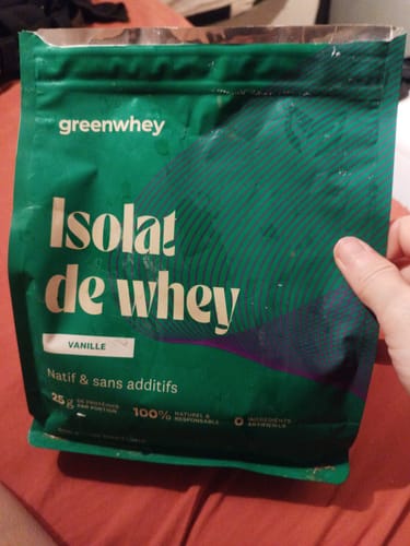 Un client tient le sachet vert ouvert de l'Isolat de whey saveur vanille dans sa main.