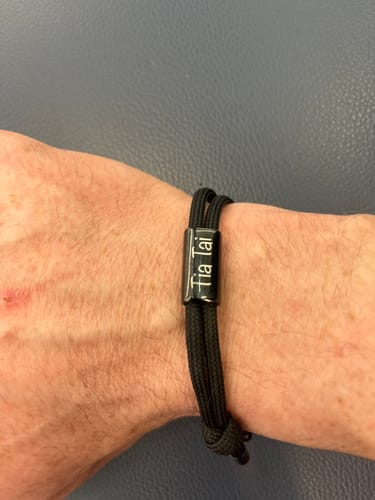 Customer's wrist wearing the black cord Sail Bracelet with an engraved pendant.