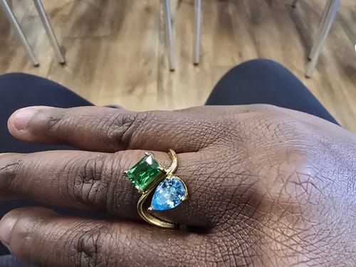 Customer's hand wearing the Navae Birthstone Ring with a green radiant-cut stone and a blue pear-cut stone.