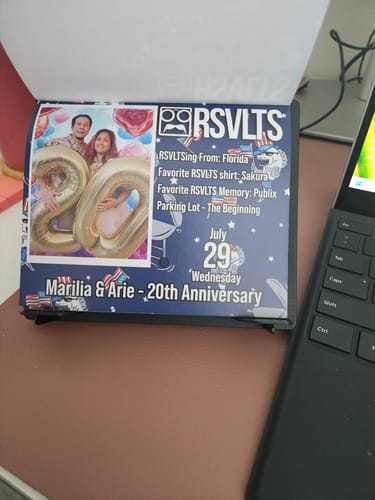 Customer's RSVLTS 2026 Calendar open on a desk. The visible page for July 29th features a couple's 20th anniversary.