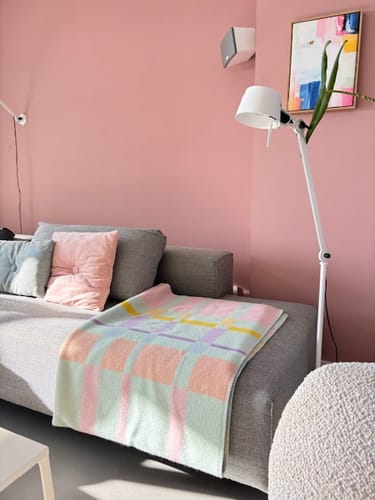 Recensent toont de mooie Røros Tweed City Plaid gedrapeerd over een grijze bank in een roze kamer.