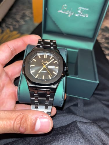 Customer holding a black Lucky Fours watch with a metal band in front of its green premium box.