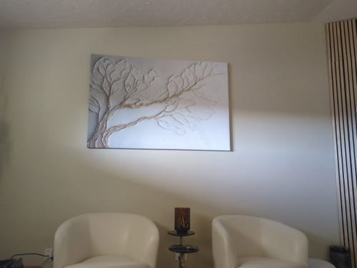 Reviewer's neutral branch canvas art hanging on a wall above two cream accent chairs, tying the room's decor together.