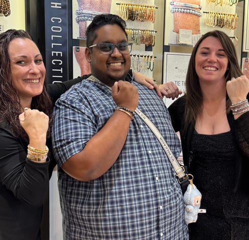 Customer smiling with two other people in a store, all proudly showing their beaded bracelets.