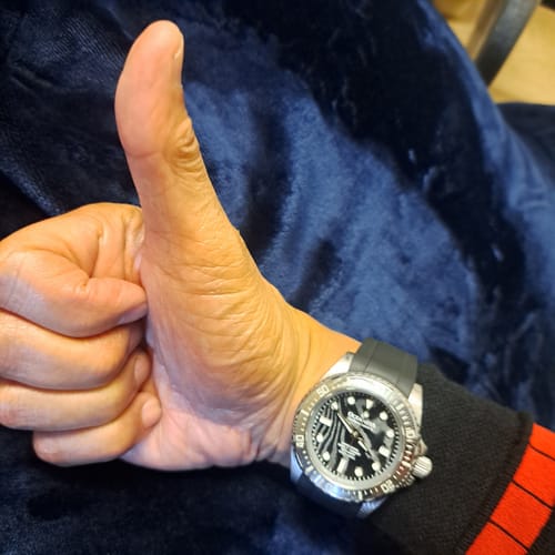 A reviewer gives a thumbs-up while wearing the Oceaneva Damascus Steel Watch, showing its patterned dial and black rubber strap.