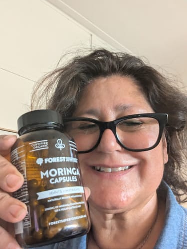 Customer smiling and holding a brown bottle of Organic Moringa Capsules.