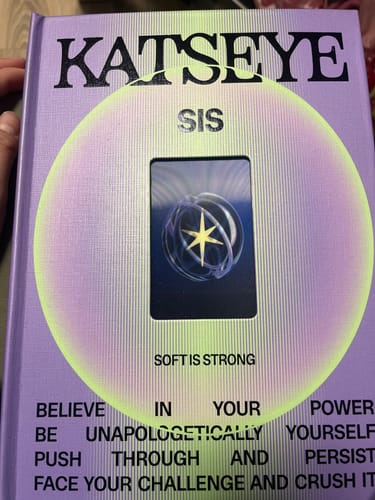 Customer holding the purple hardcover Katseye SIS album, showing the front with its central cutout window and card.