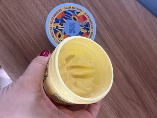 Cliente segurando o pote aberto de Creme BB, mostrando a textura do creme amarelo por dentro.