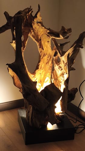 Ein Kunde zeigt die von innen beleuchtete Treibholz Stehlampe VILLA. Das Holz steht auf einem schwarzen Sockel auf dem Boden.