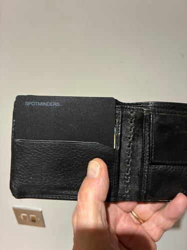 Customer holding an open black wallet, showing the SPOTMINDERS. Tracking Card neatly fitting inside a slot.