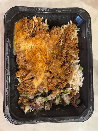 Close-up of a customer's prepared Taco Bowl in its black container, showing ground turkey, cheese, and rice.