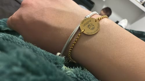 Customer showing a gold-colored bracelet with a personalized round pendant on their wrist.