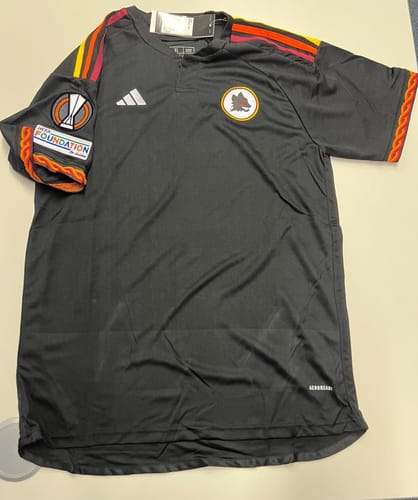 Il cliente mostra la parte anteriore della maglia nera dell'EUROPA LEAGUE stesa su una superficie.